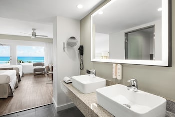 A modern hotel room with a large bed, a desk, a chair, a flat-screen TV, and a balcony with a view of the ocean. at Hotel Riu Plaza Miami Beach