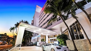 A modern hotel entrance with a white car parked in front, palm trees, and a clear sky. - Hotel Riu Plaza Miami Beach (Miami Beach)