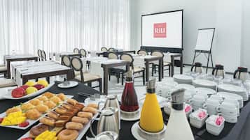 Un salón de conferencias con mesas dispuestas para una reunión, una pantalla de proyector y una pizarra.