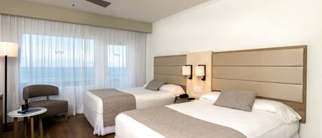 A hotel room with two beds, a desk, a chair, a ceiling fan, and a window with curtains.