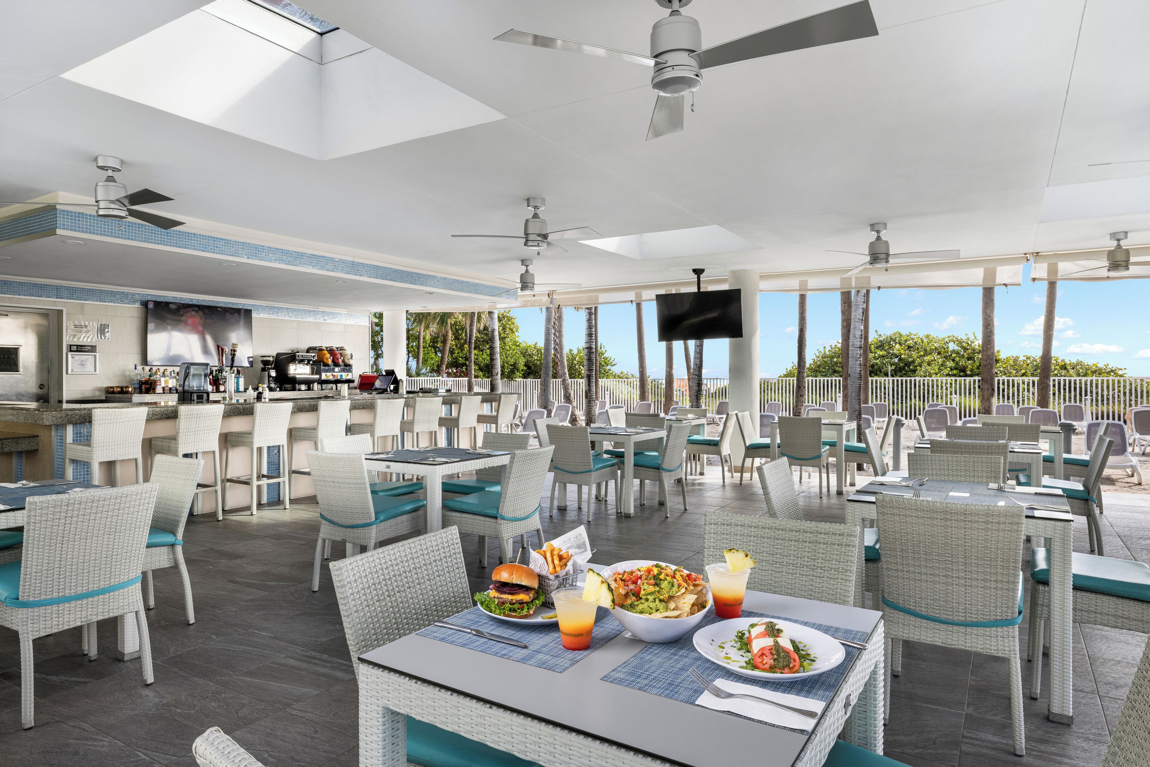 A spacious outdoor dining area with wicker furniture, a bar, and a TV screen.
