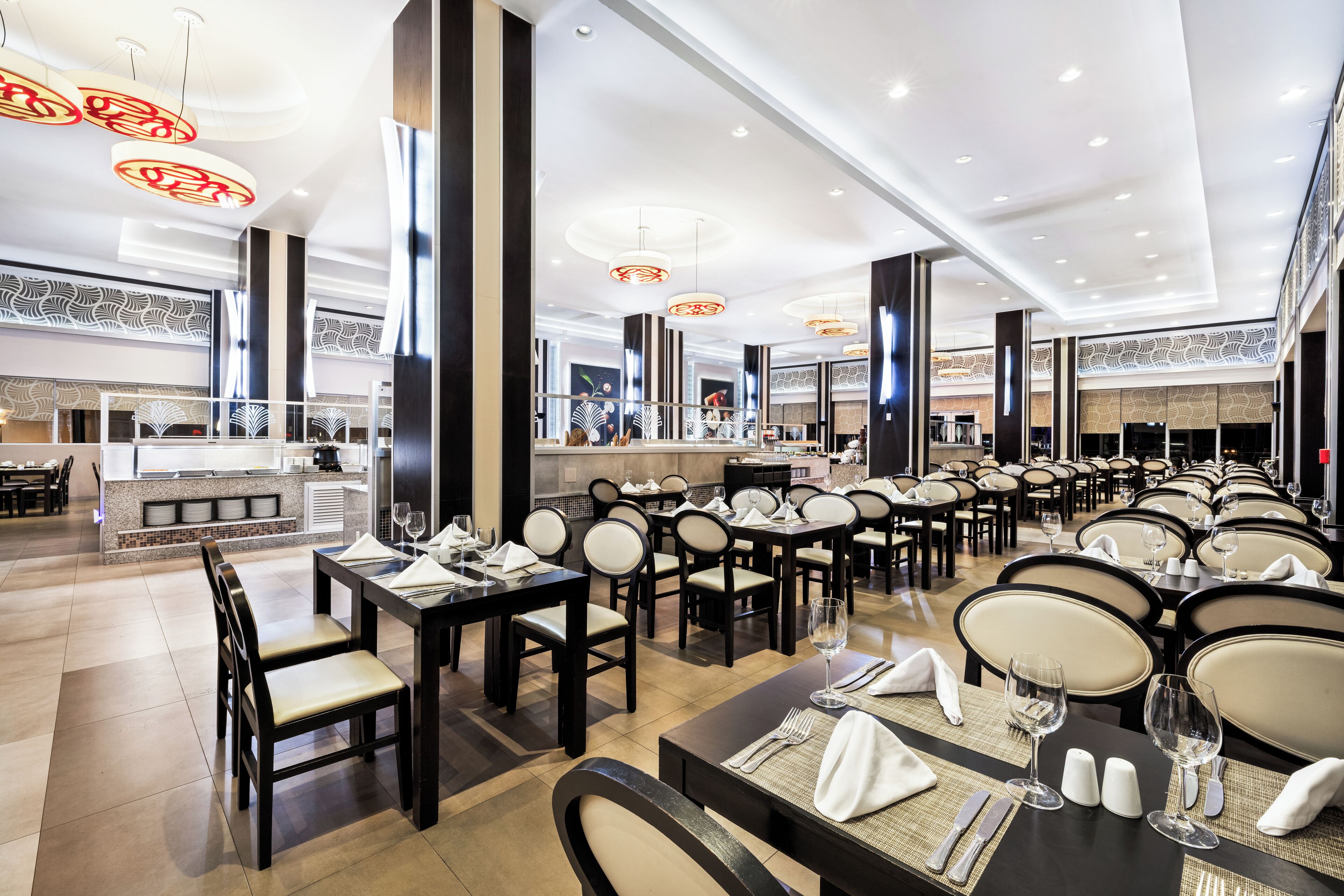 A spacious dining area with multiple tables and chairs, a central bar, and a modern ceiling design.