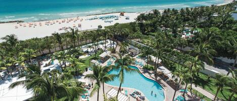 A resort with a central pool, beach, and palm trees.