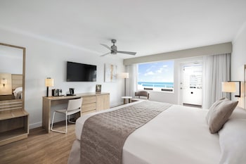 A lobby with a beige sofa, two armchairs, and a coffee table. There are two tall, narrow vases on either side of the sofa. at Hotel Riu Plaza Miami Beach