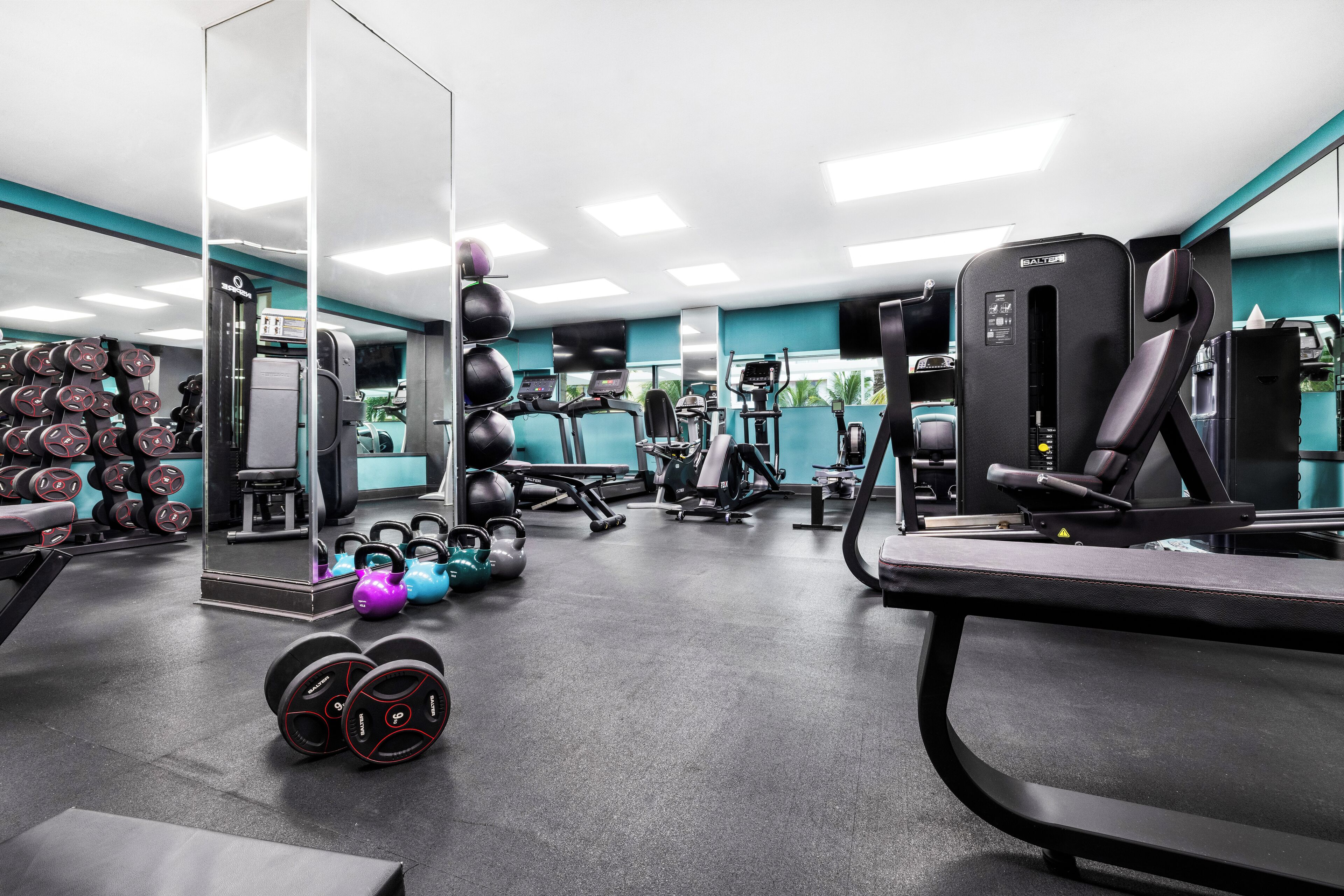 A gym with various exercise equipment, including dumbbells, kettlebells, and cardio machines.