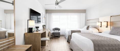 A modern hotel room with a large bed, a desk with a chair, a small table, a ceiling fan, and a large window with curtains.