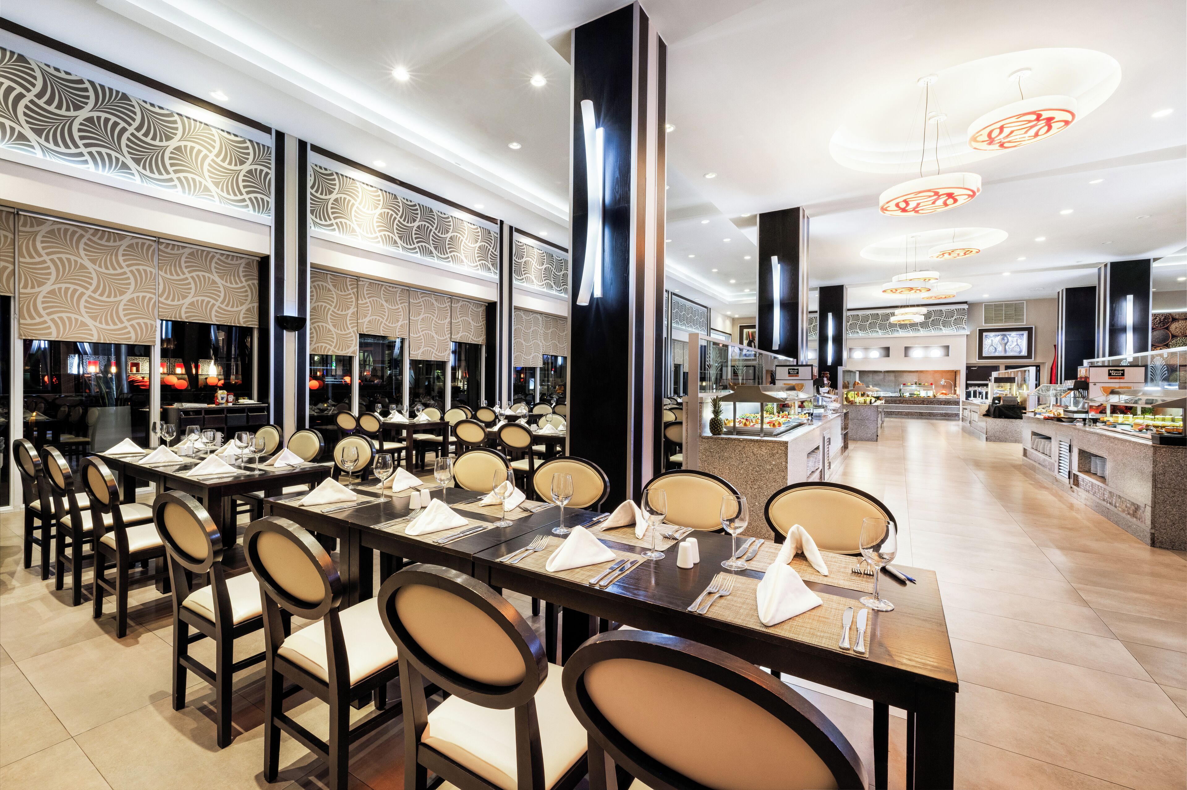 A modern restaurant with long tables, chairs, and a buffet area.