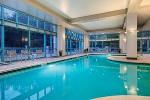 An indoor swimming pool with clear glass walls, multiple seating areas, and a tiled deck.