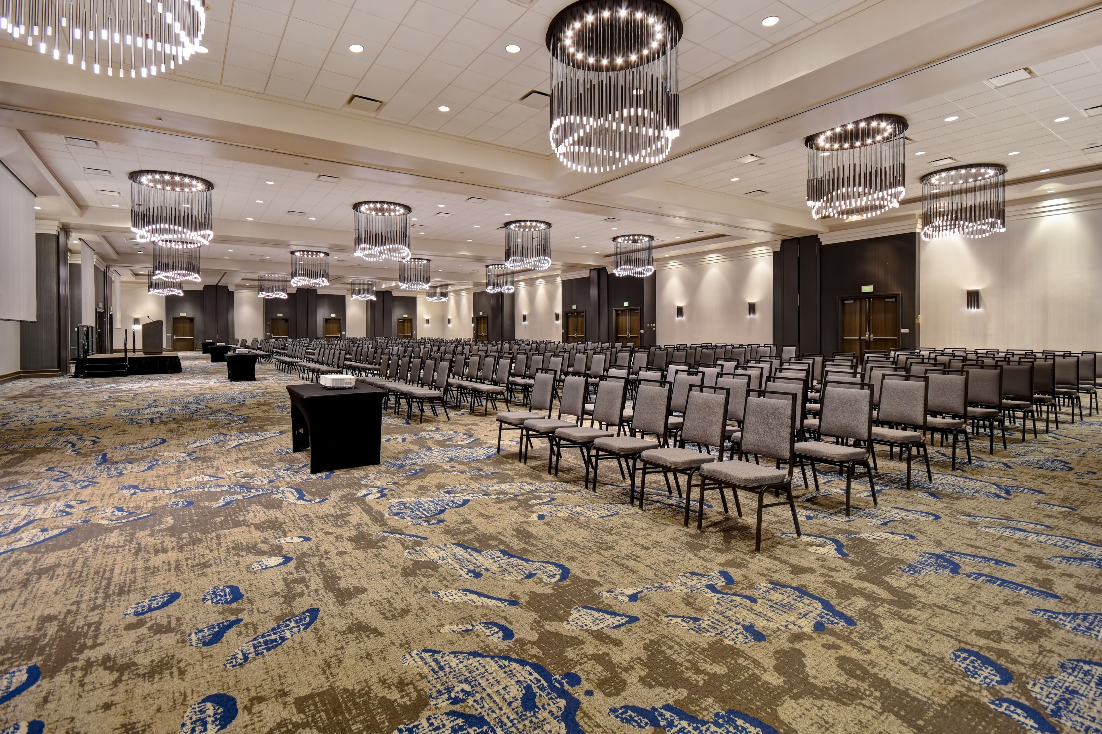 A large conference room with rows of chairs, a podium, and modern chandeliers.