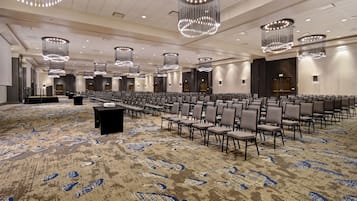 A large conference room with rows of chairs, a podium, and modern chandeliers.