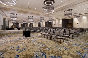 Une grande salle de conférence avec des rangées de chaises, un pupitre et des lustres modernes.