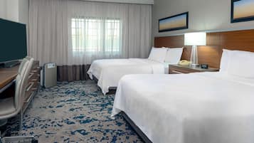 A hotel room with two beds, a desk, a chair, a TV, and a window with curtains.