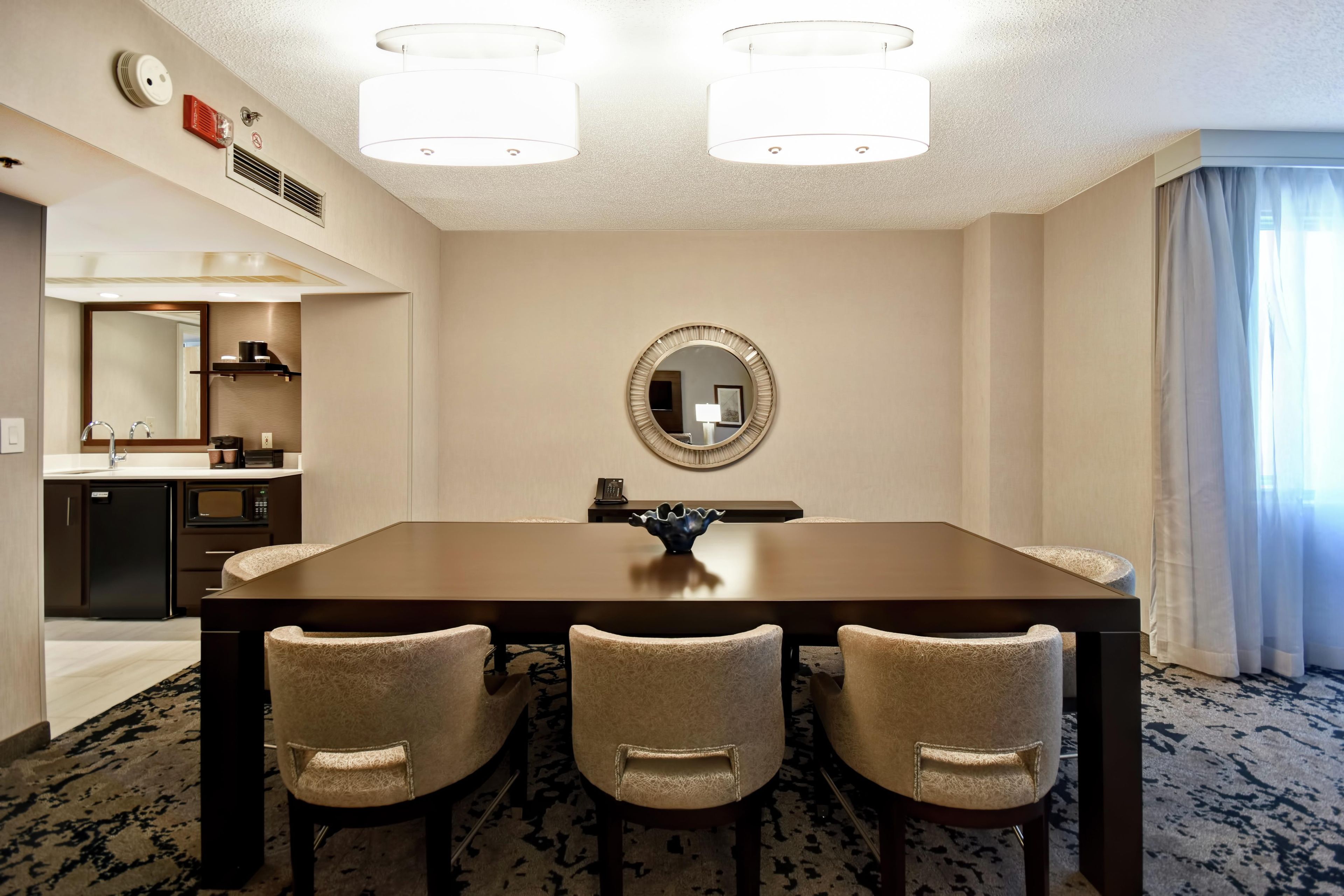 A hotel room with a dining area featuring a wooden table and three upholstered chairs.