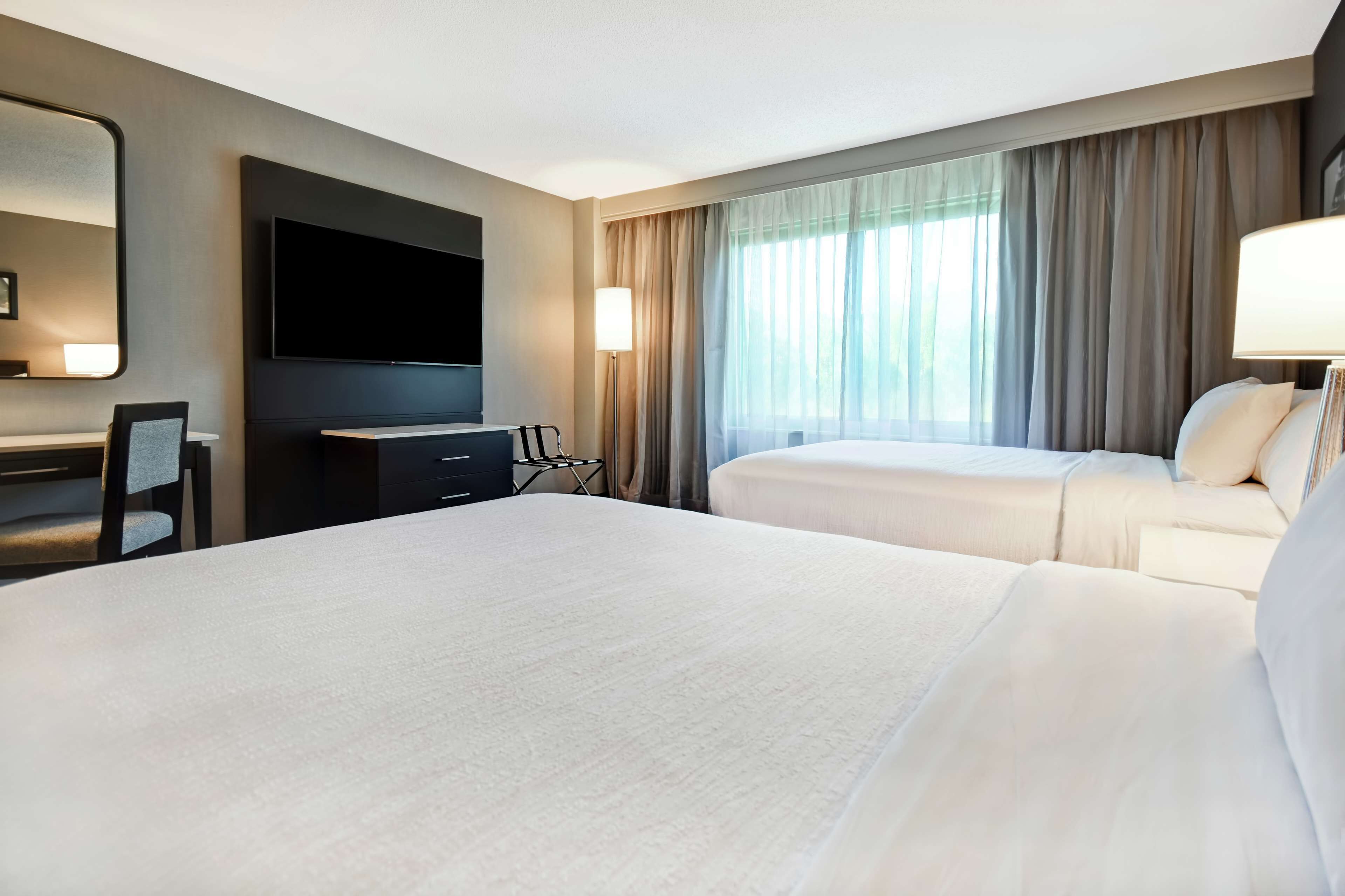Une chambre d’hôtel avec deux lits, un bureau, une chaise, une télévision et une fenêtre avec des rideaux.