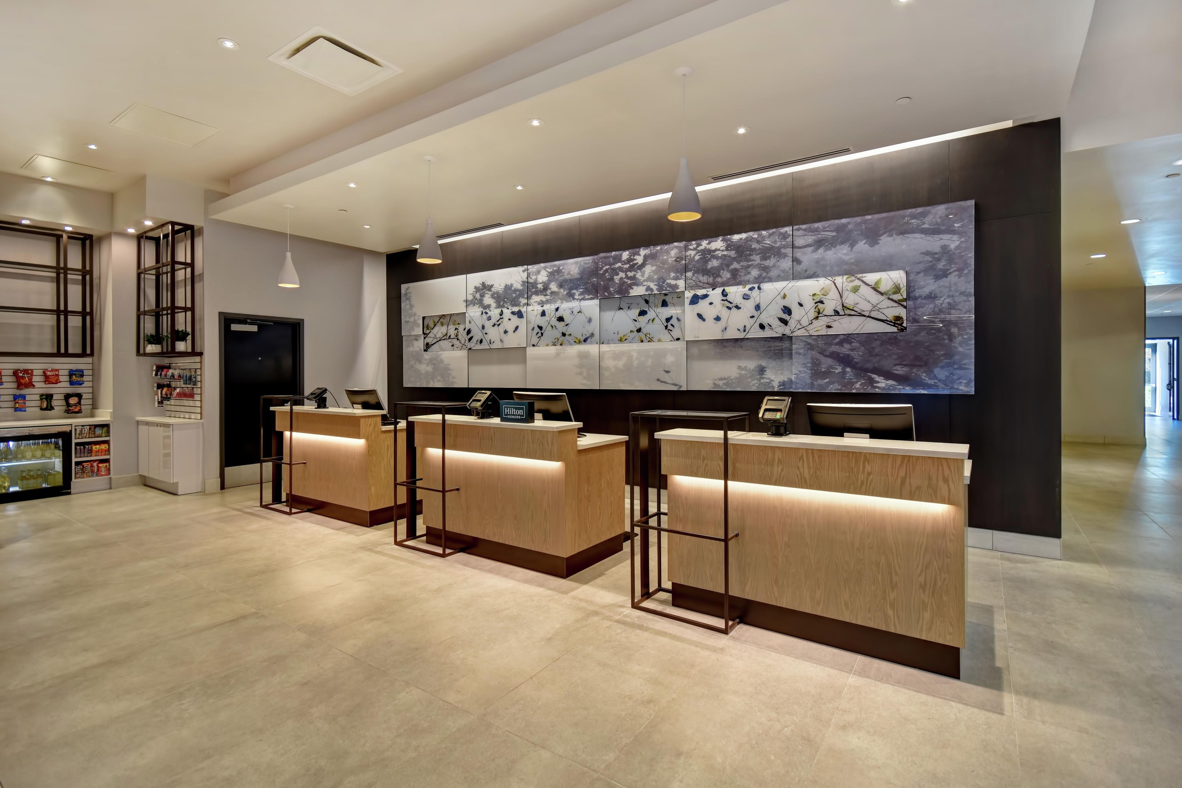 A hotel reception area with three wooden reception desks, a large wall-mounted artwork, and a minibar.