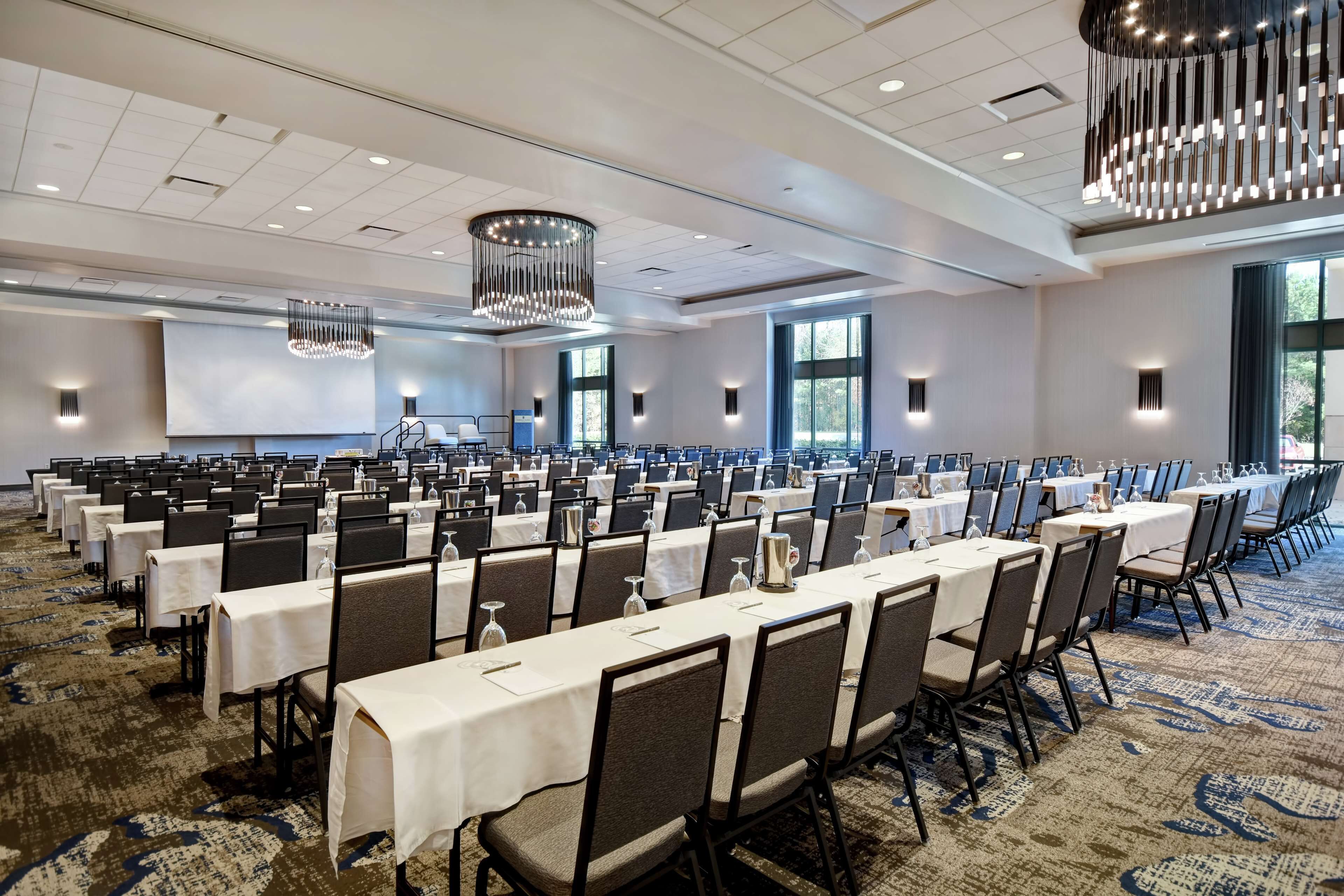 A large conference room with rows of tables and chairs, chandeliers, and large windows.