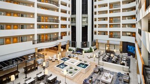 Eine mehrstöckige Hotelhalle mit einem zentralen Atrium, mehreren Essbereichen und einem großen Bildschirm.
