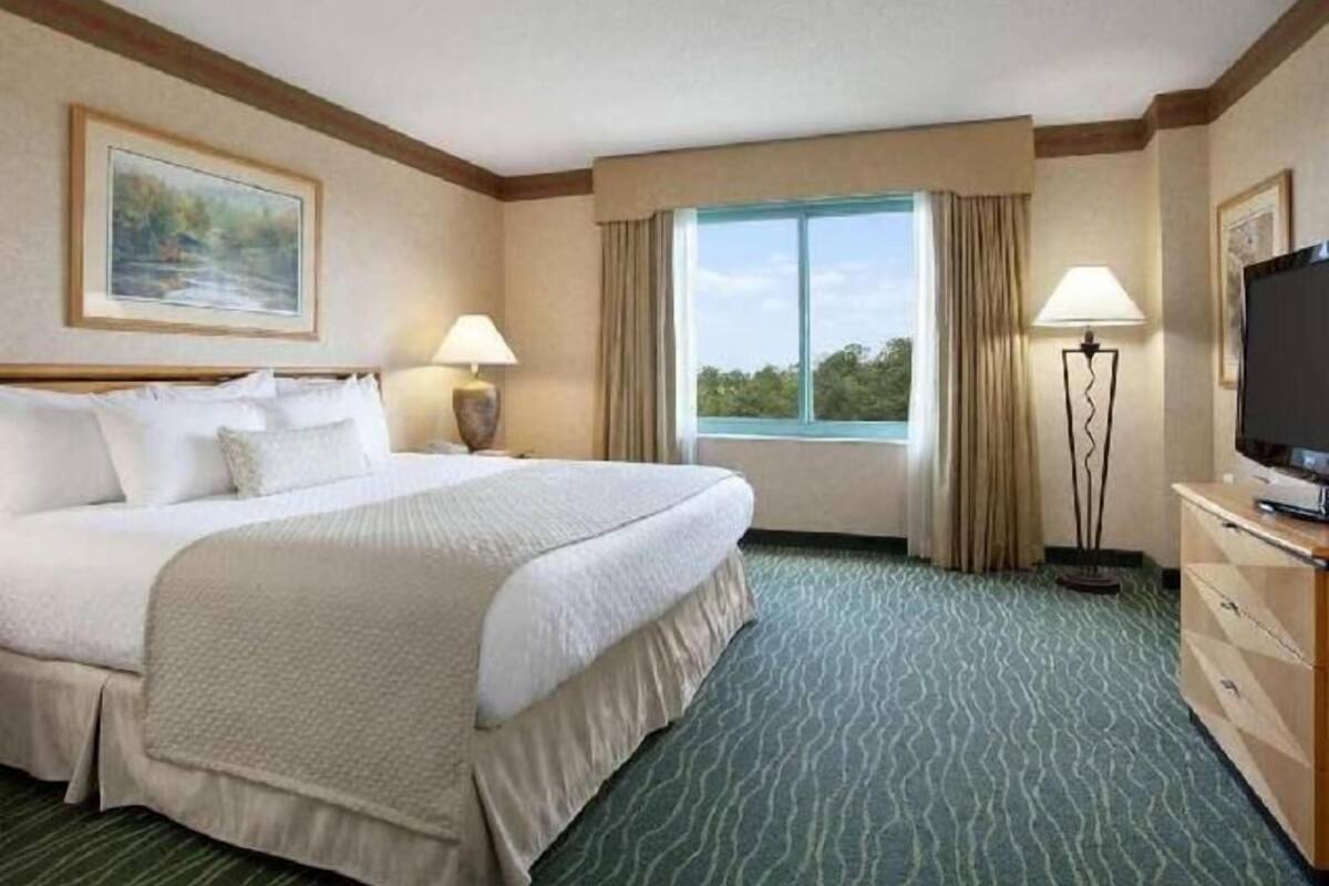A hotel room with a large bed, a desk with a television, a window with curtains, and a painting on the wall.
