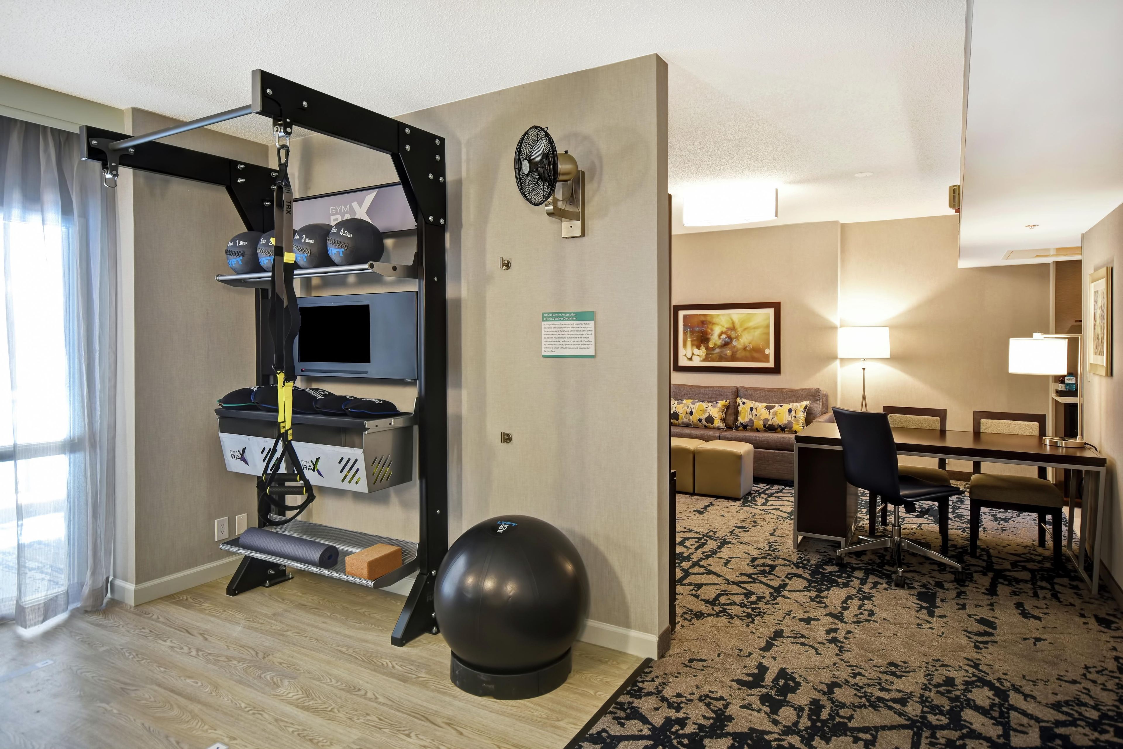 A hotel room with a pull-up bar, exercise ball, and a desk with a chair.