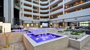 Eine moderne Hotelhalle mit einer zentralen Wasserspüle, mehreren Etagen und verschiedenen Sitzbereichen.