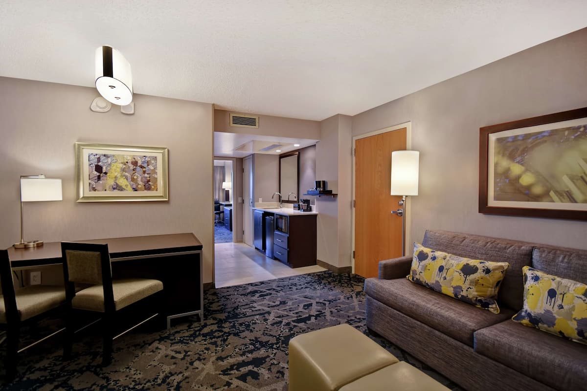 A hotel room with a desk, a sofa, a patterned rug, and artwork on the walls.