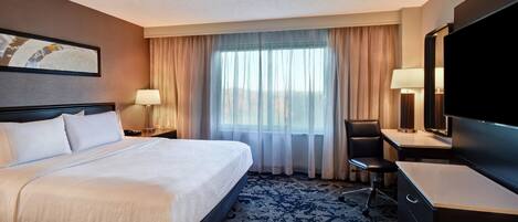 A hotel room with a bed, a desk, a chair, a TV, and a window with curtains.