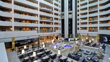 A multi-level hotel lobby with a central atrium, multiple dining areas, and a pool.