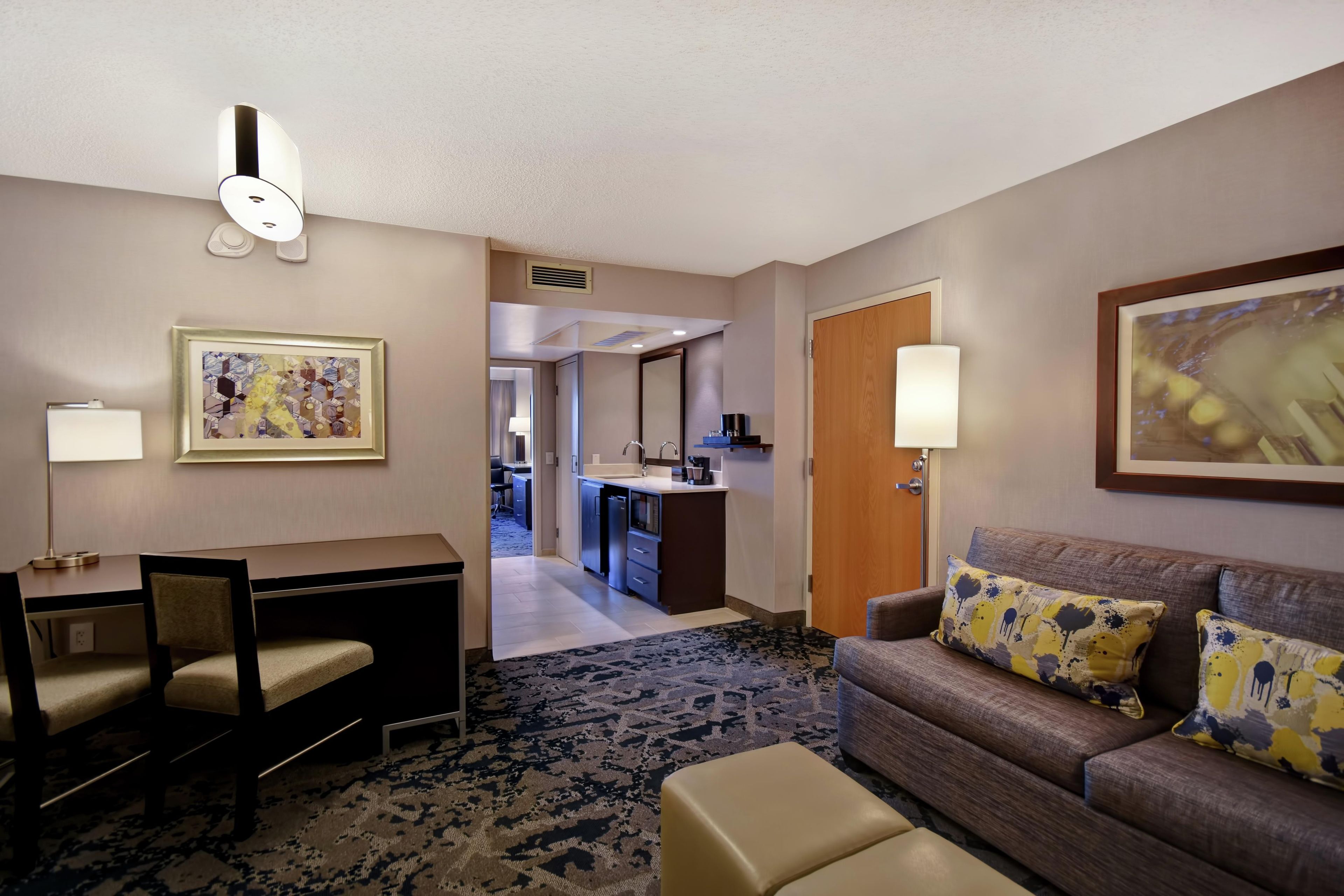 A hotel room with a desk, a sofa, a patterned rug, and artwork on the walls.