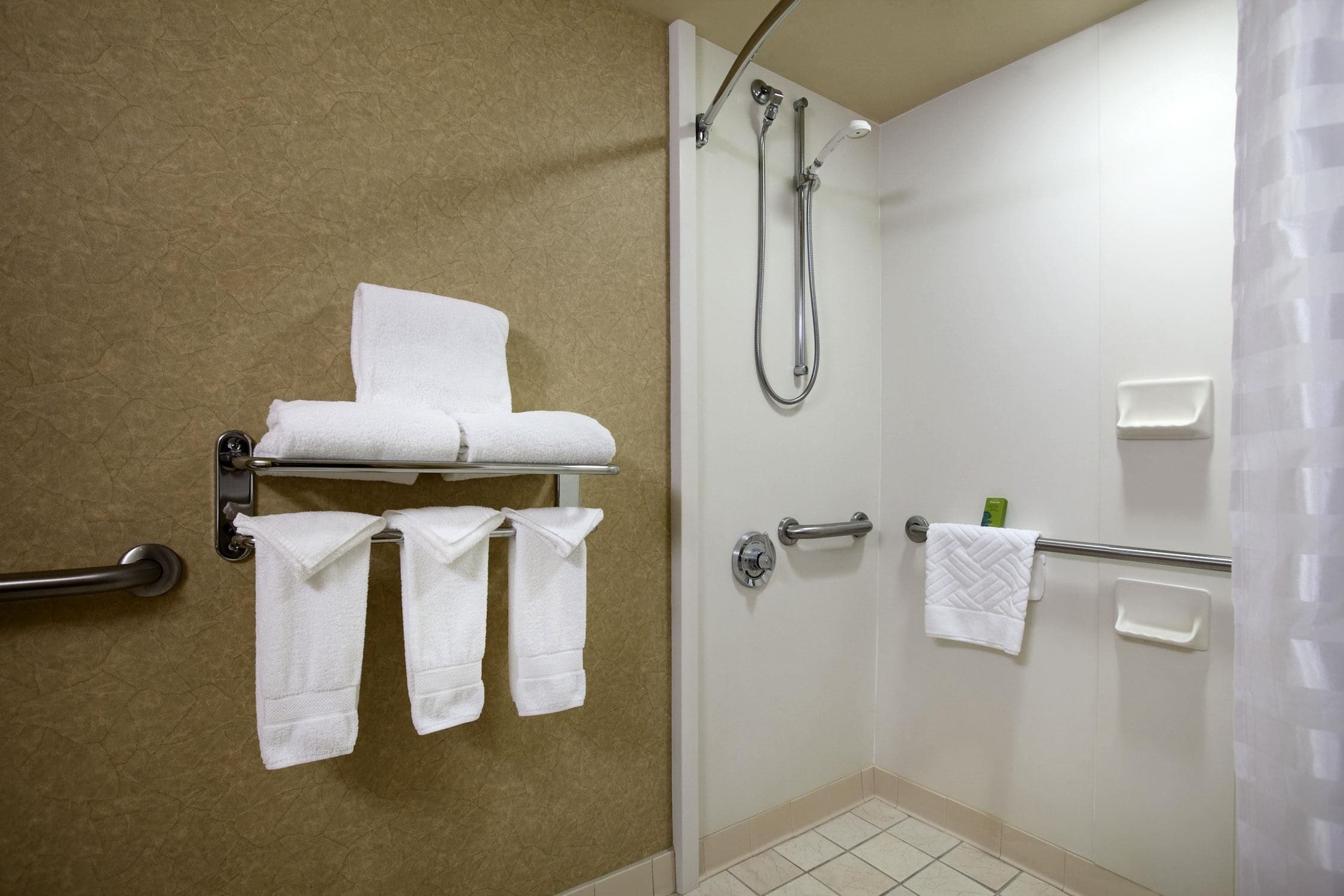 A bathroom with a shower, a towel rack with multiple towels, and a toilet paper holder.