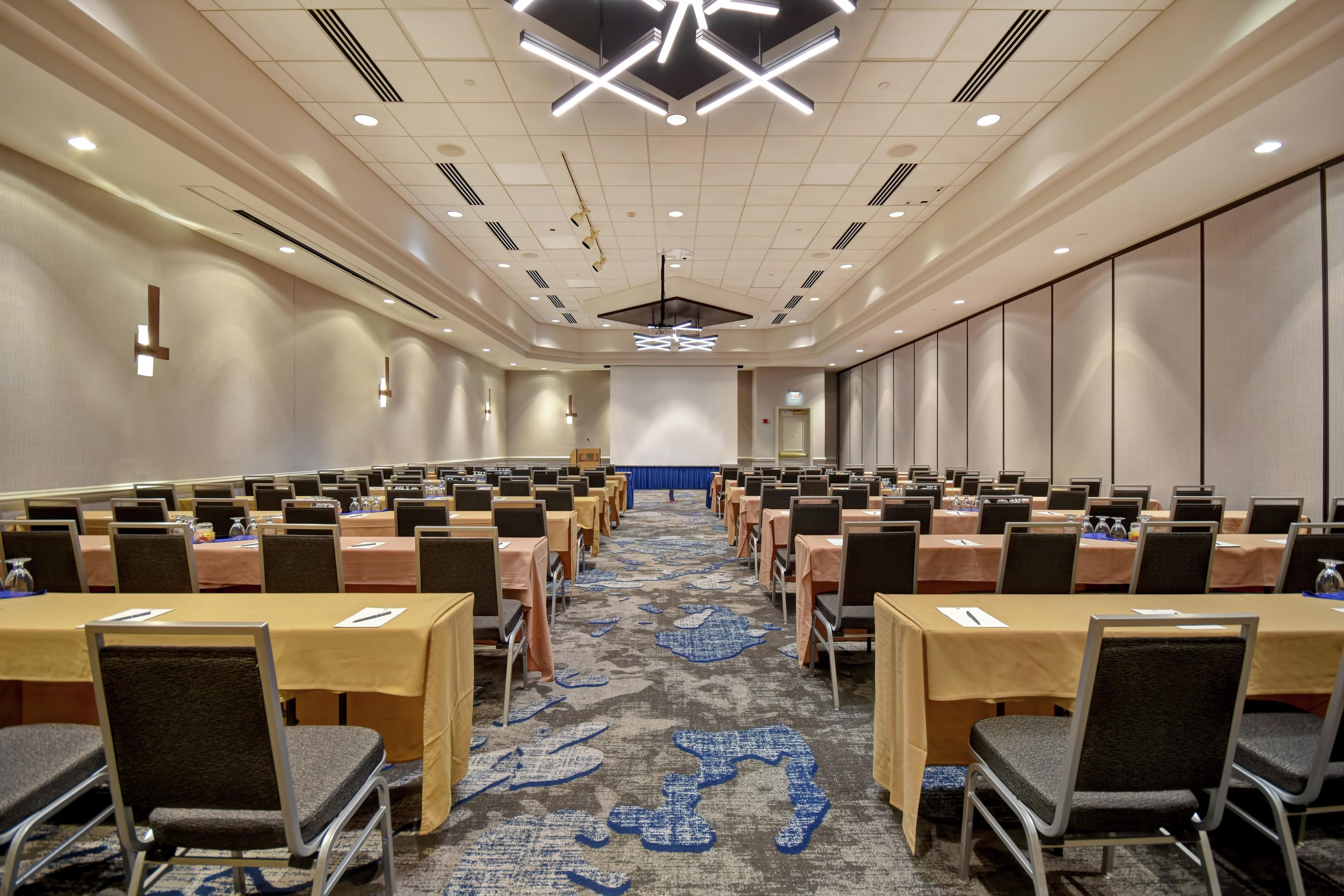 A conference room with rows of tables and chairs, a patterned carpet, and a modern ceiling design.