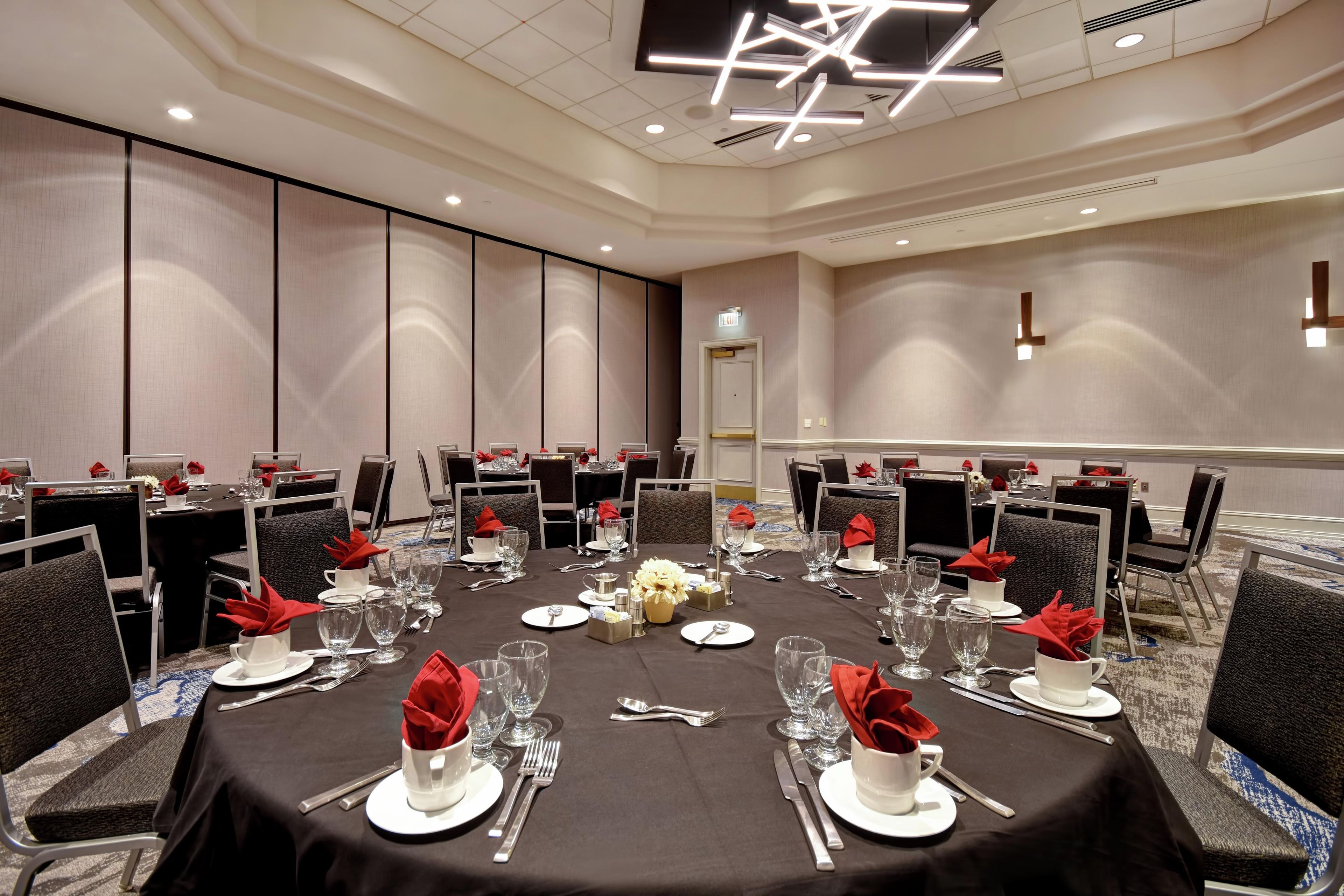 Une salle de conférence avec des tables rondes disposées pour un repas, équipée de couverts, de verres et de serviettes.