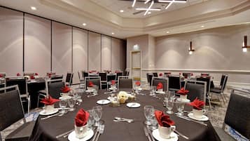 Une salle de conférence avec des tables rondes disposées pour un repas, équipée de couverts, de verres et de serviettes.