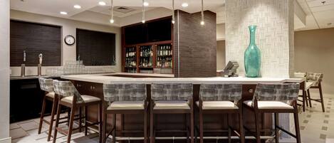 A modern bar area with a high bar counter, multiple stools, and a large decorative vase.