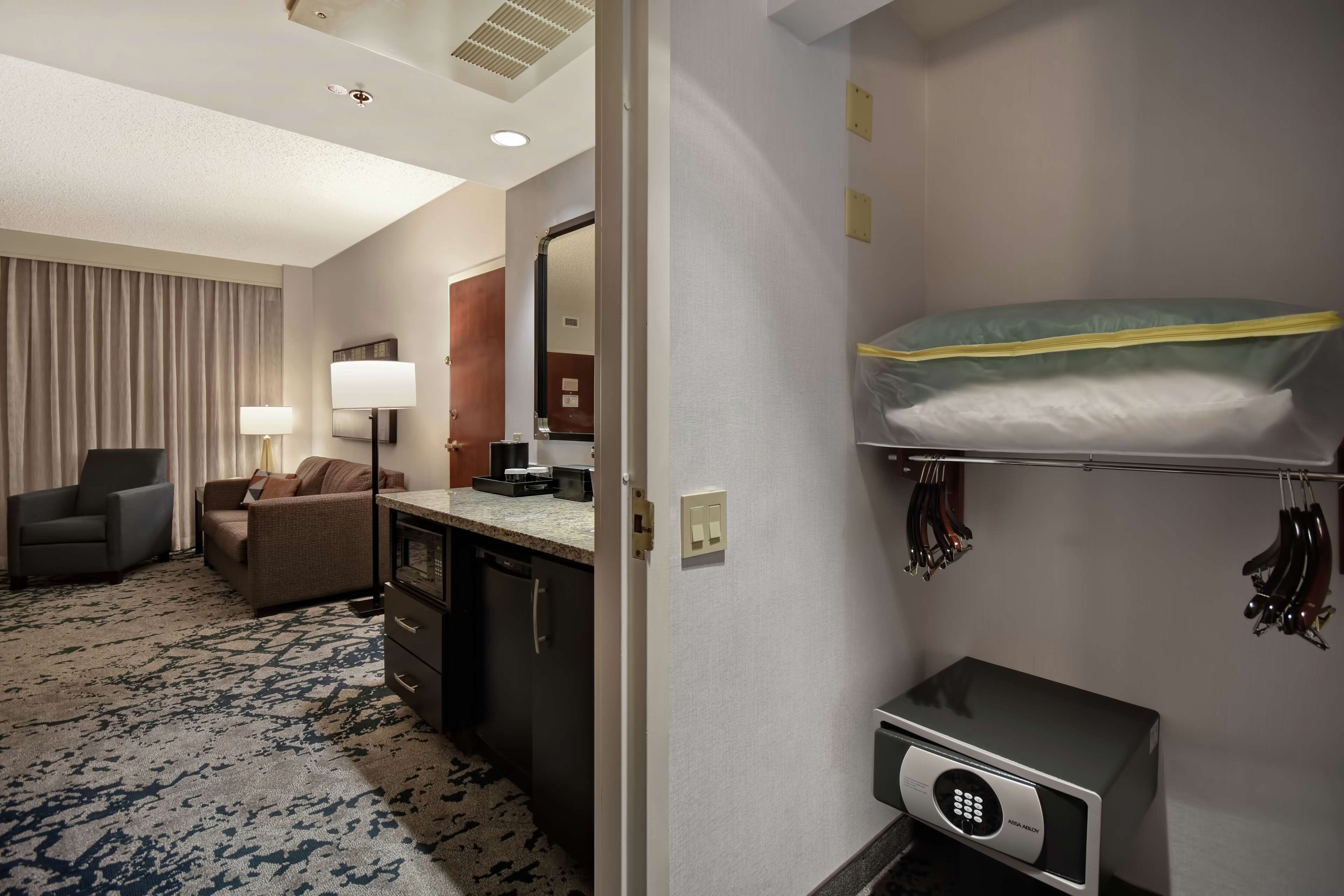 A hotel room with a bunk bed, a desk with a computer, a chair, a sofa, a lamp, and a wardrobe.