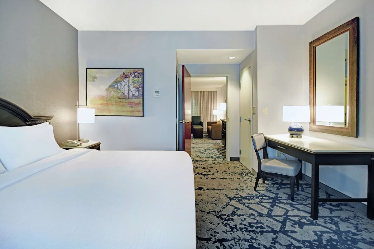 A hotel room with a bed, desk, chair, and a large mirror.
