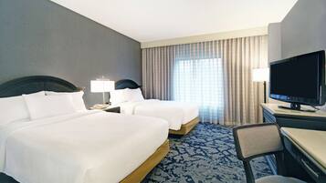 A hotel room with two beds, a desk with a television, and a chair.