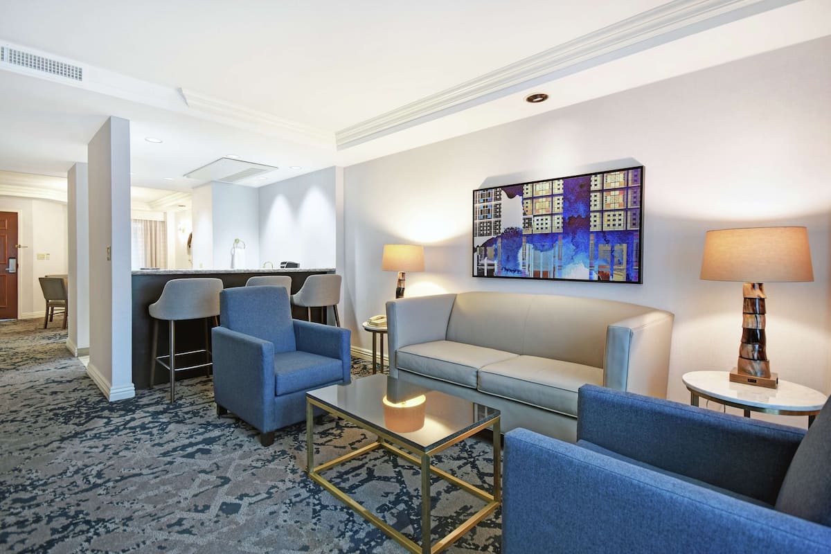 A modern hotel lobby with a seating area, a dining area, and a large wall art piece.
