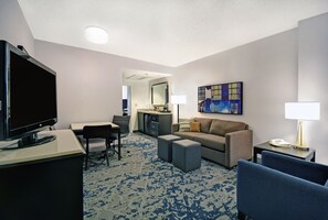 A hotel room with a flat-screen TV, a sofa, a desk, a chair, a small kitchenette, and a painting on the wall. - Embassy Suites Charleston (Charleston)