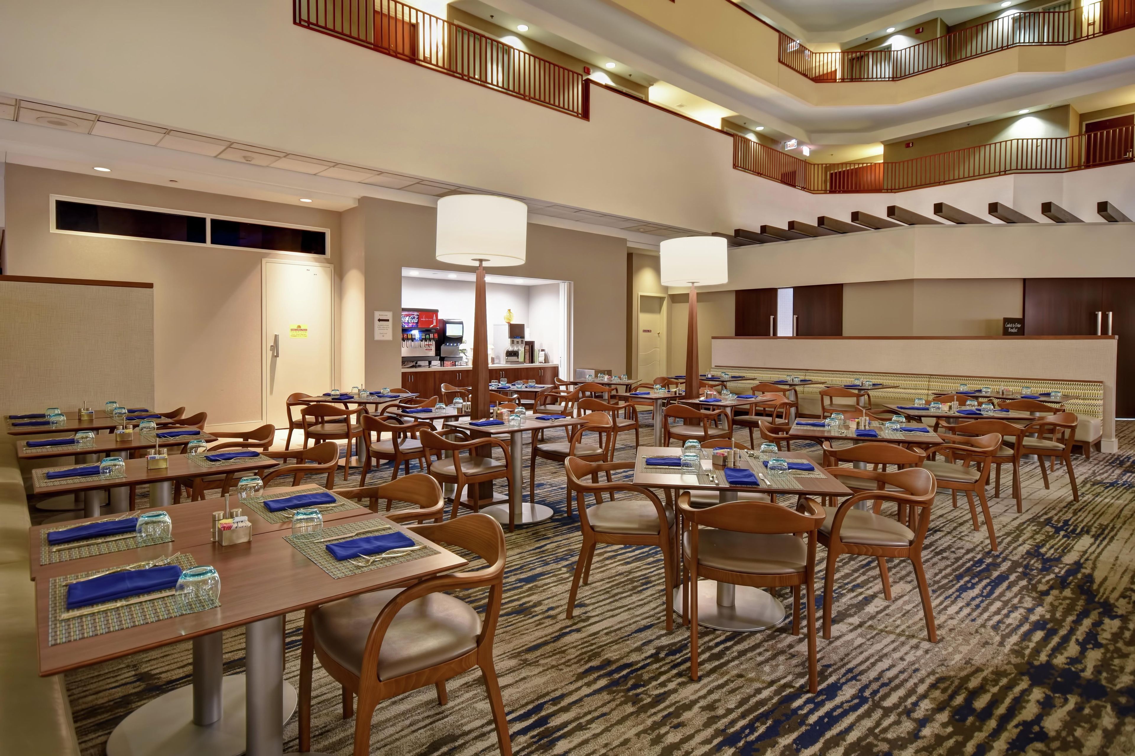 A hotel dining area with multiple tables and chairs, a central service desk, and a staircase connecting the floors.