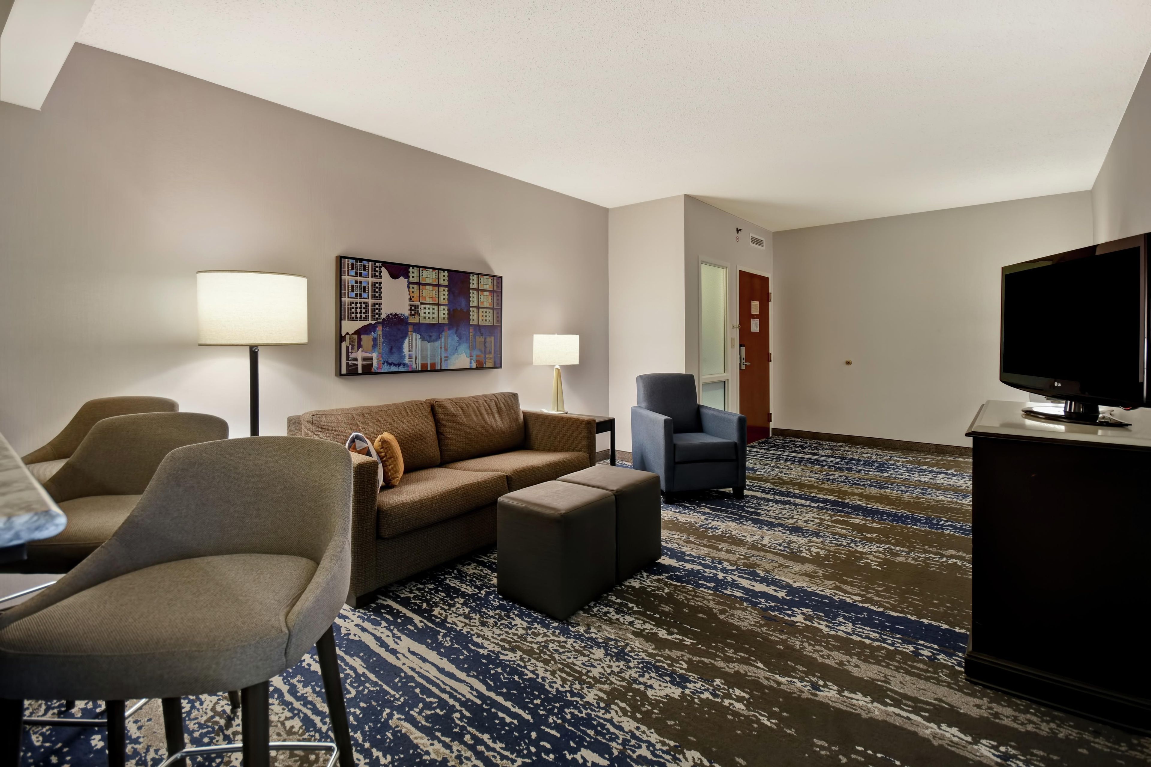 A hotel room with a sofa, armchairs, a television, and a painting on the wall.