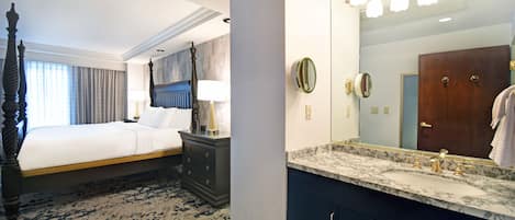 A hotel room with a bed, a nightstand with a lamp, a large mirror, and a marble bathroom vanity.