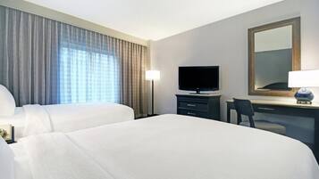 Habitación de hotel con dos camas, un escritorio, un televisor y un espejo grande.