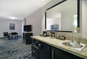A hotel room with a kitchenette, a television, a dining area with a chair and table, and artwork on the walls. - Embassy Suites Charleston (Charleston)