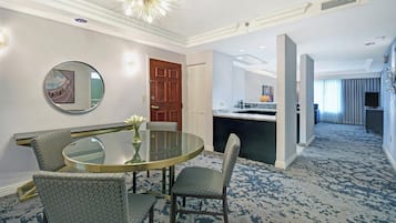 Habitación de hotel con una mesa de vidrio redonda, dos sillas con estampado, una puerta de madera, un espejo y vistas al pasillo.
