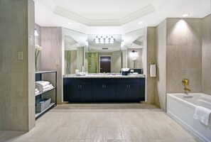 A modern bathroom with a large mirror, dark cabinets, a bathtub, and a shelf with towels.