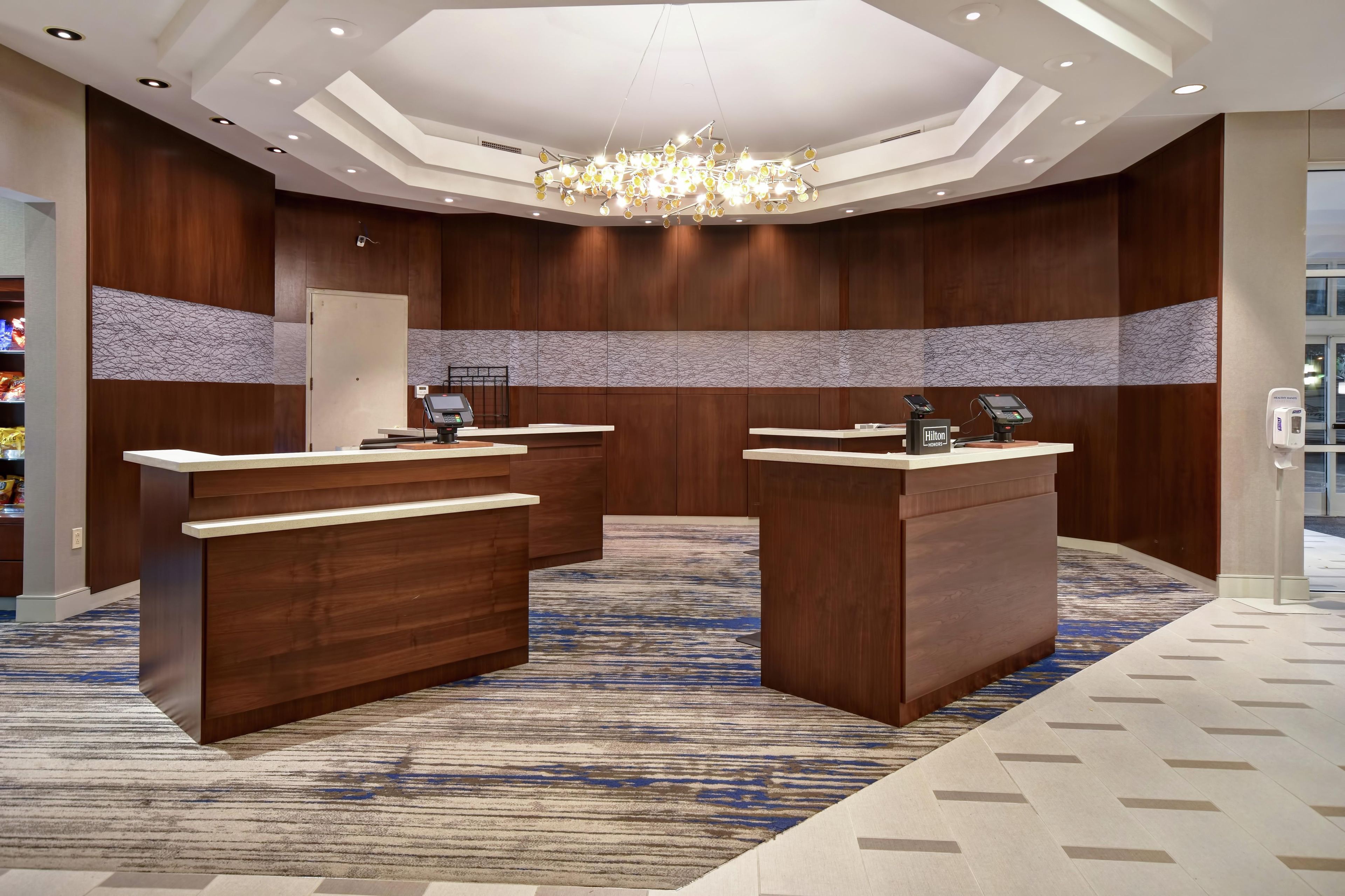 A hotel reception area with a modern design, featuring a chandelier, wooden reception desks, and a patterned carpet.