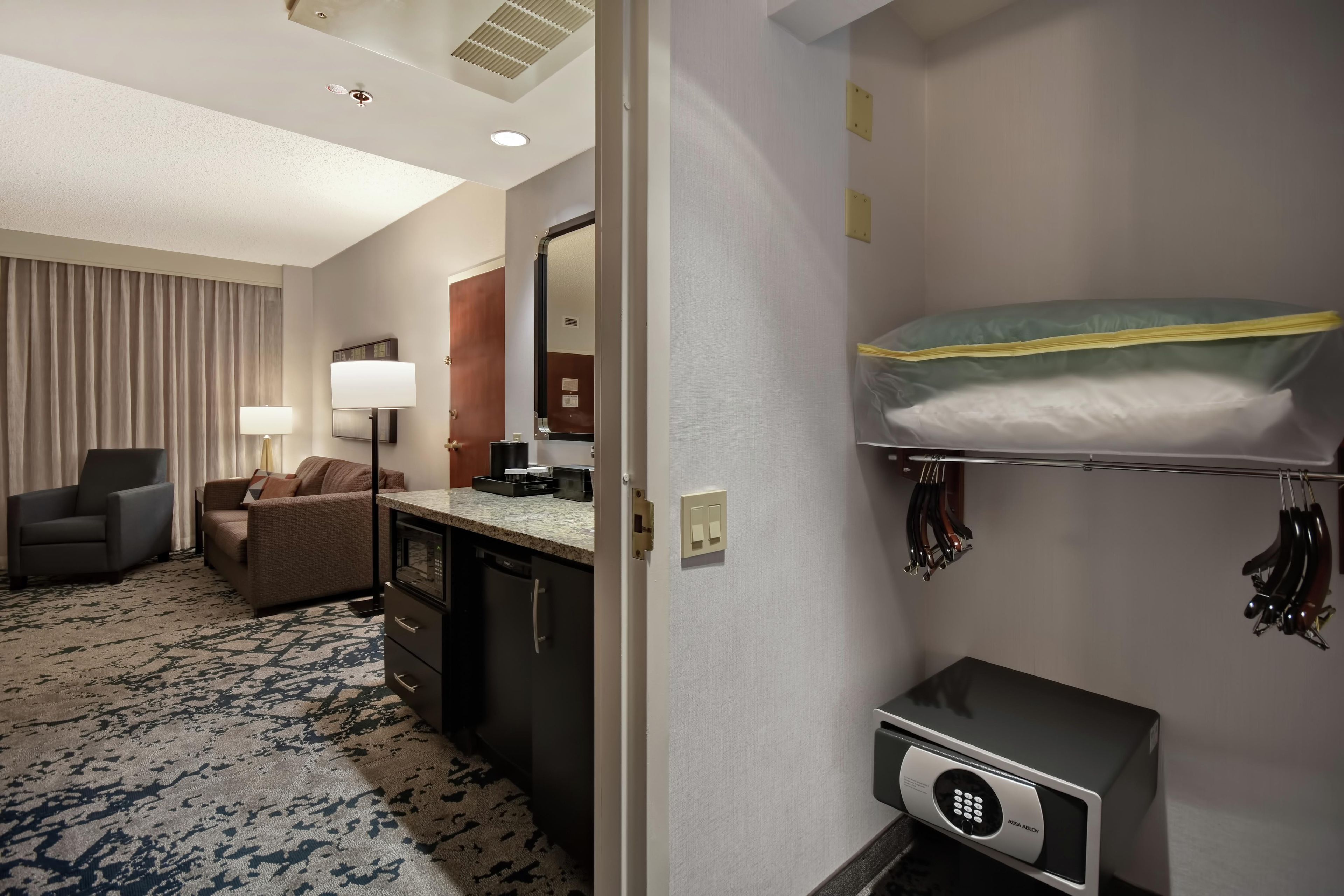 A hotel room with a bunk bed, a desk with a lamp, a chair, a sofa, and a minibar.