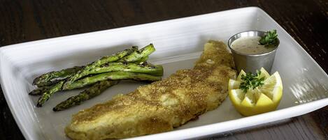 Prato branco retangular com filé de peixe empanado, aspargos e um gomo de limão, acompanhado por uma pequena xícara de molho.