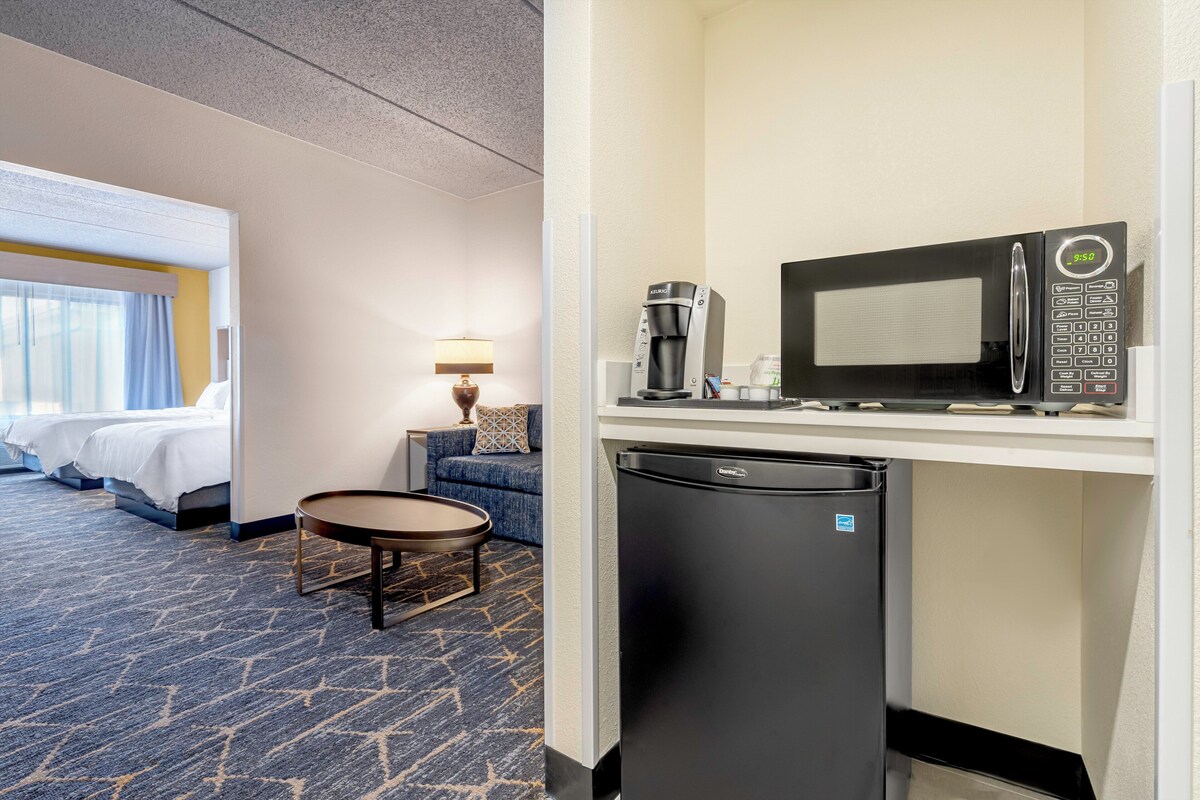 A hotel room with a bed, a sofa, a coffee maker, a microwave, and a mini-fridge.