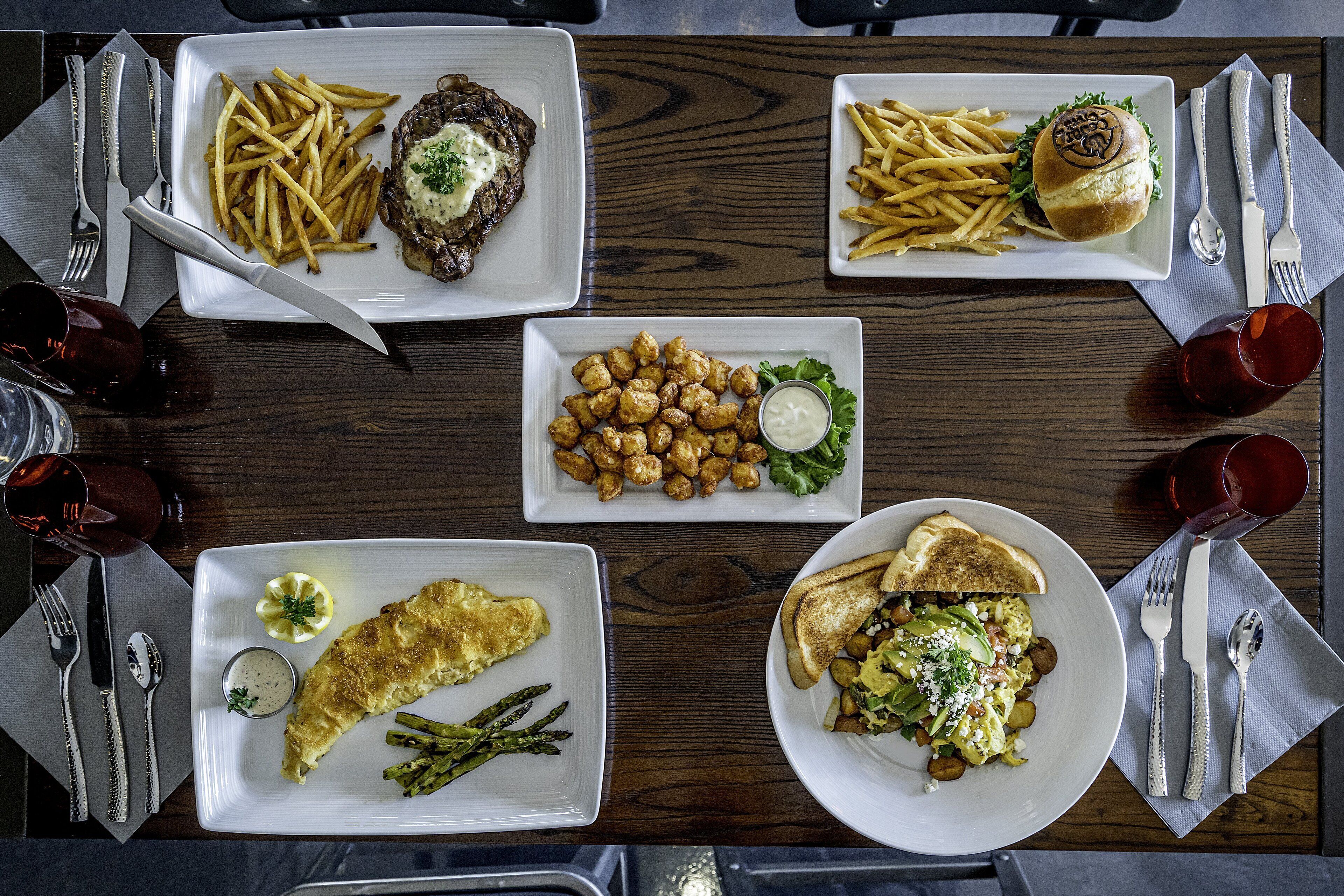 Una mesa de comedor con diversos platos, incluyendo filete, papas fritas, nuggets de pollo y un sándwich.